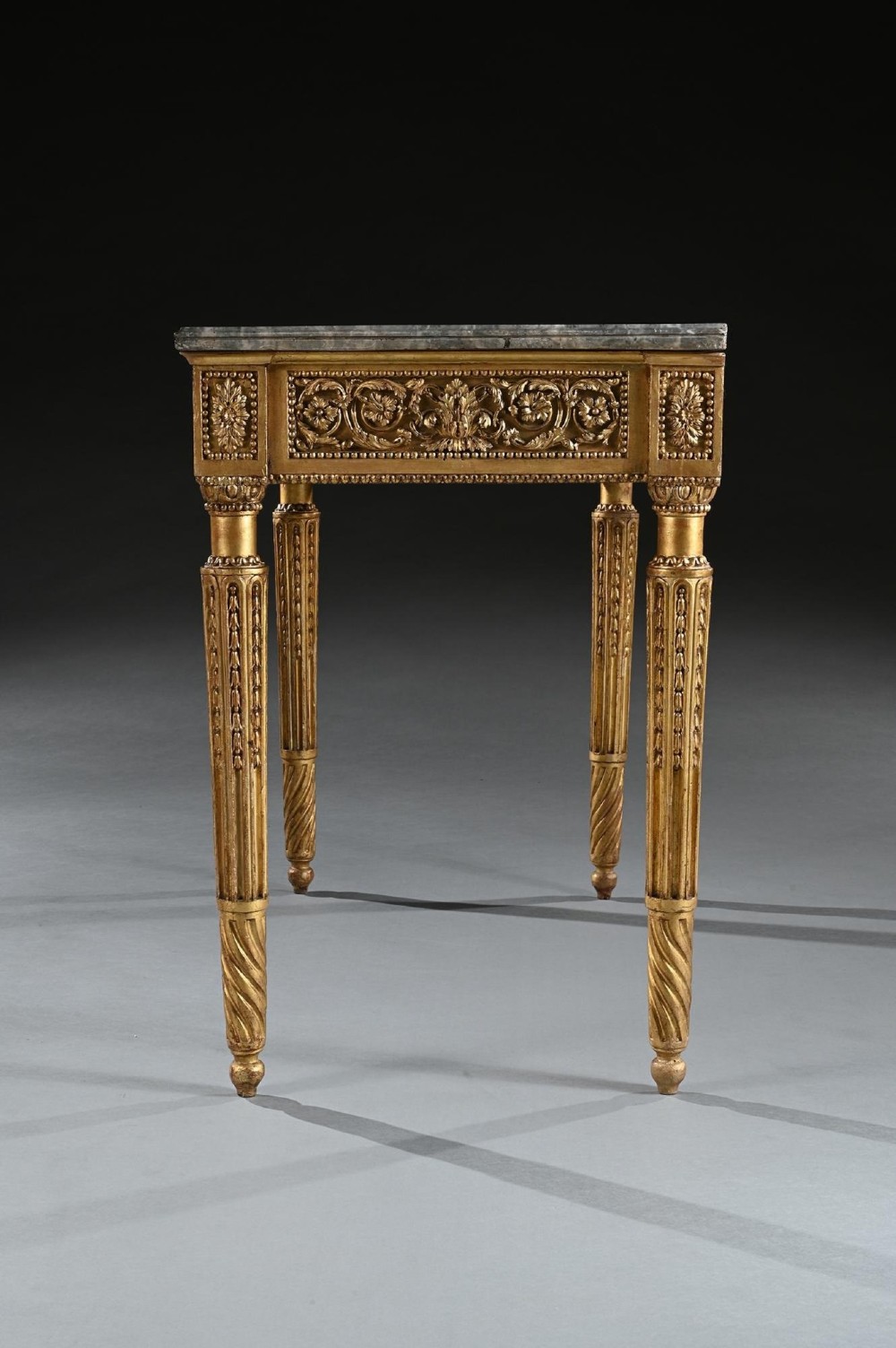 An 18th-century Italian Neoclassical console table featuring a grey veined marble top, an intricate giltwood frieze with a central carved mask, and fluted legs. View V