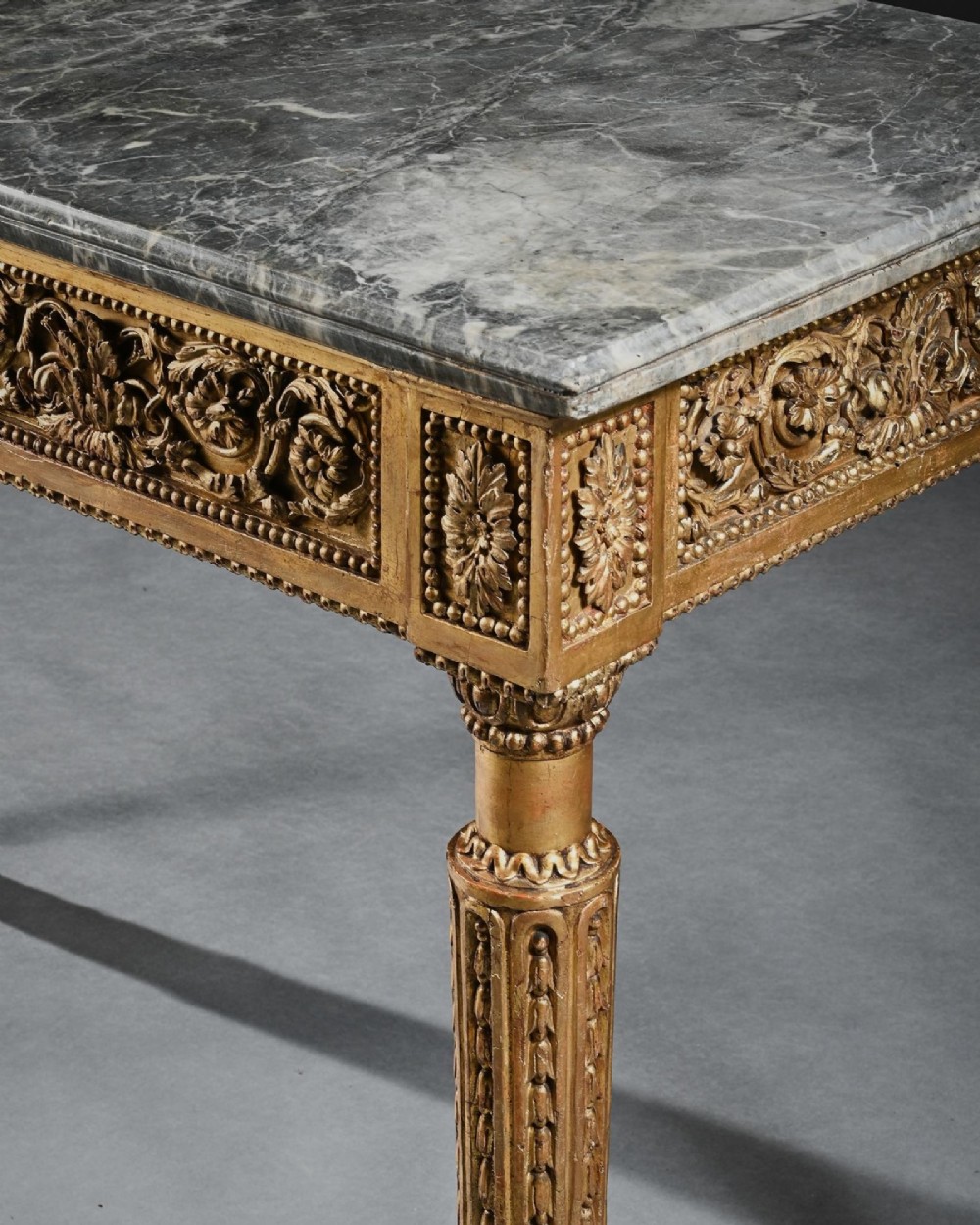 An 18th-century Italian Neoclassical console table featuring a grey veined marble top, an intricate giltwood frieze with a central carved mask, and fluted legs. View VII