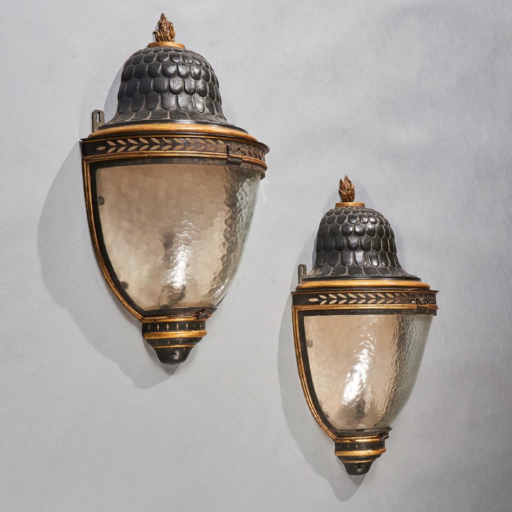 A pair of early 19th-century French tole peinte wall lanterns featuring imbricated scale domes, flame finials, and parcel gilt leaf borders over curved textured glass. View II