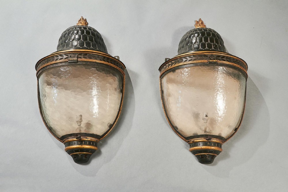 A pair of early 19th-century French tole peinte wall lanterns featuring imbricated scale domes, flame finials, and parcel gilt leaf borders over curved textured glass. View V