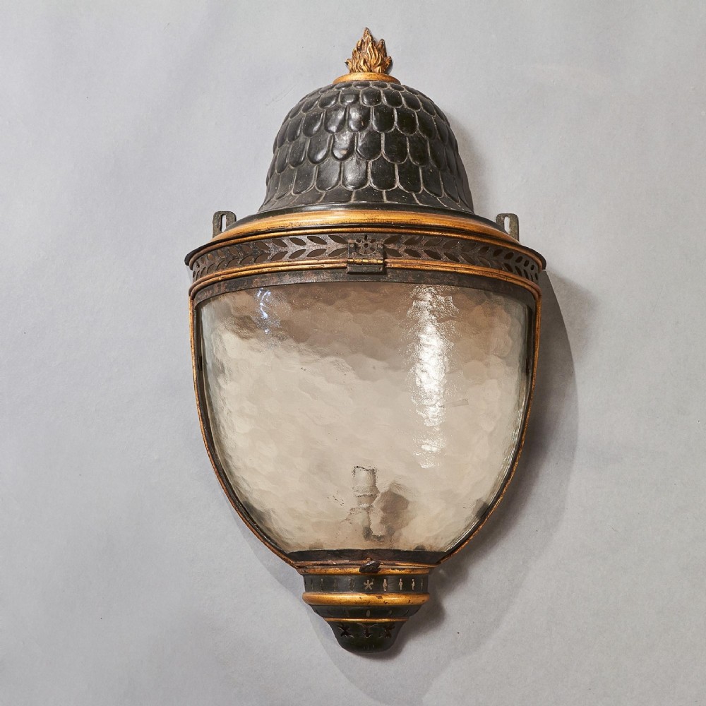 A pair of early 19th-century French tole peinte wall lanterns featuring imbricated scale domes, flame finials, and parcel gilt leaf borders over curved textured glass. View VI