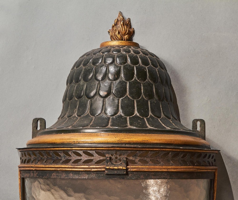 A pair of early 19th-century French tole peinte wall lanterns featuring imbricated scale domes, flame finials, and parcel gilt leaf borders over curved textured glass. View VII