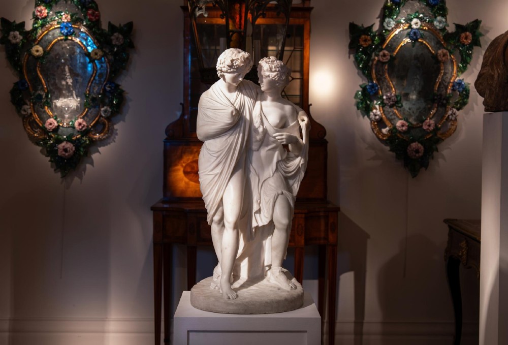 A hand-carved white marble Neoclassical sculpture depicting the classical mythological figures of Bacchus and Ariadne standing together on a circular integral base. View V