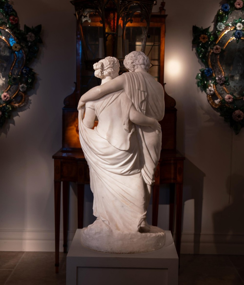 A hand-carved white marble Neoclassical sculpture depicting the classical mythological figures of Bacchus and Ariadne standing together on a circular integral base. View IX