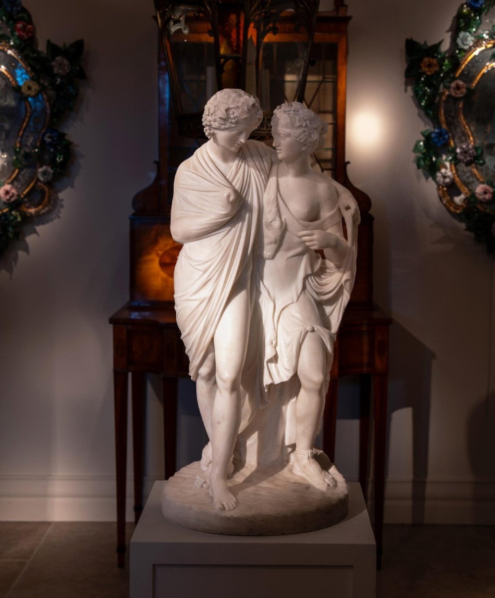 A hand-carved white marble Neoclassical sculpture depicting the classical mythological figures of Bacchus and Ariadne standing together on a circular integral base. View X