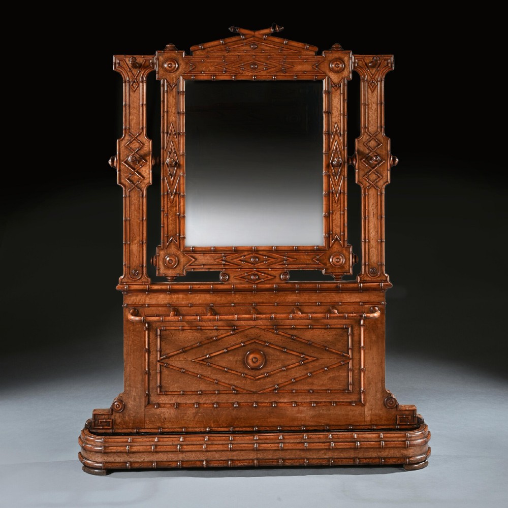 A late 19th-century French Aesthetic Period hall stand made from birdseye maple featuring turned faux bamboo detailing, a central rectangular mirror, coat hooks, geometric carved panelling, and an umbrella rack base.