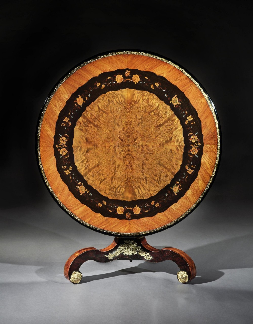 A 19th-century circular marquetry centre table featuring floral wood inlays, a tilt-top mechanism, and a dark carved tripod base with gilt-bronze mounts. View II