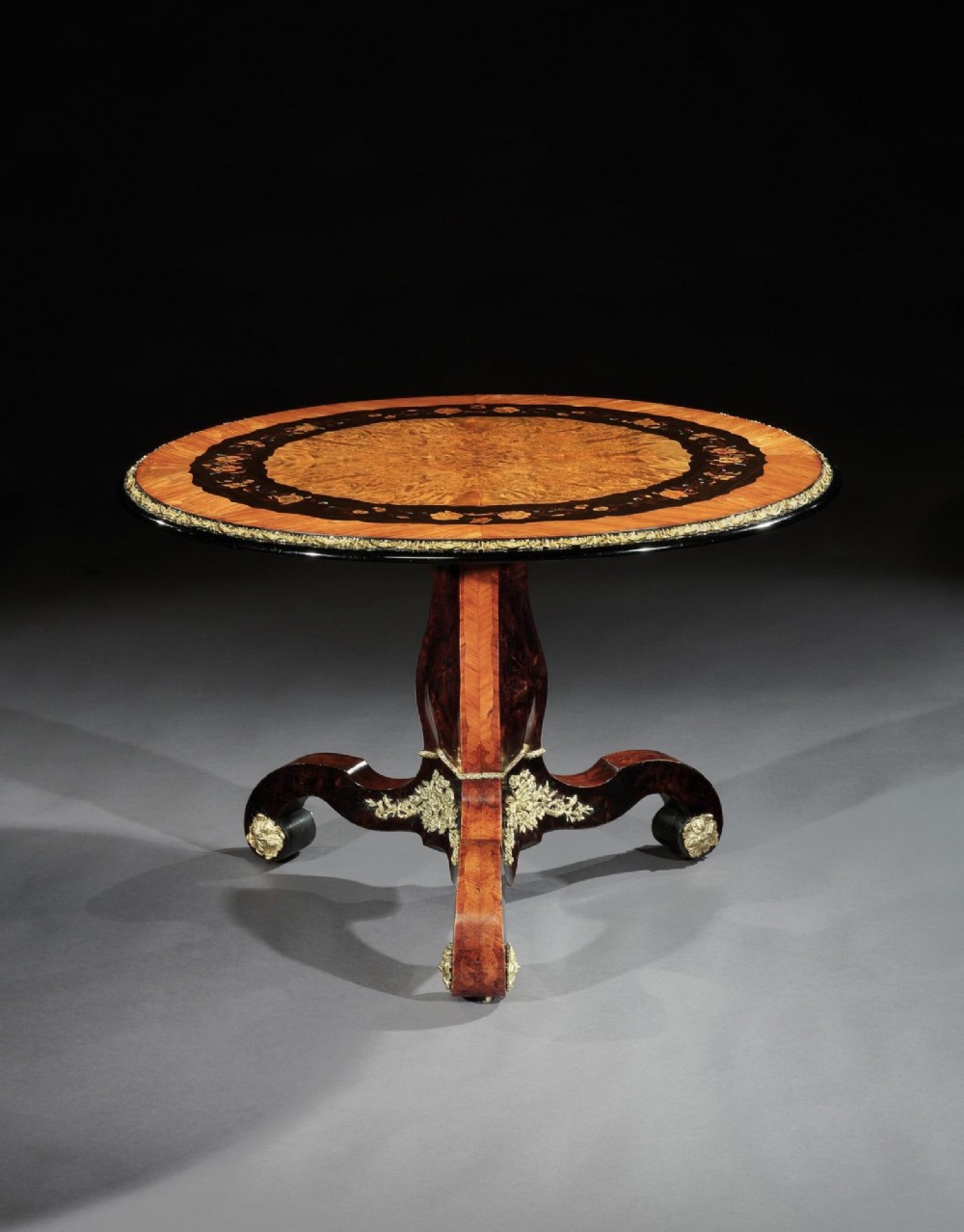 A 19th-century circular marquetry centre table featuring floral wood inlays, a tilt-top mechanism, and a dark carved tripod base with gilt-bronze mounts. View III