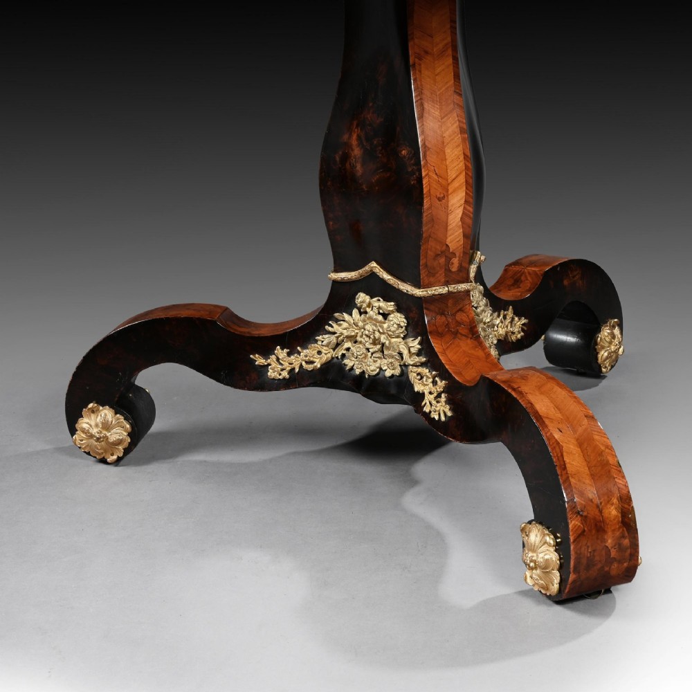 A 19th-century circular marquetry centre table featuring floral wood inlays, a tilt-top mechanism, and a dark carved tripod base with gilt-bronze mounts. View V