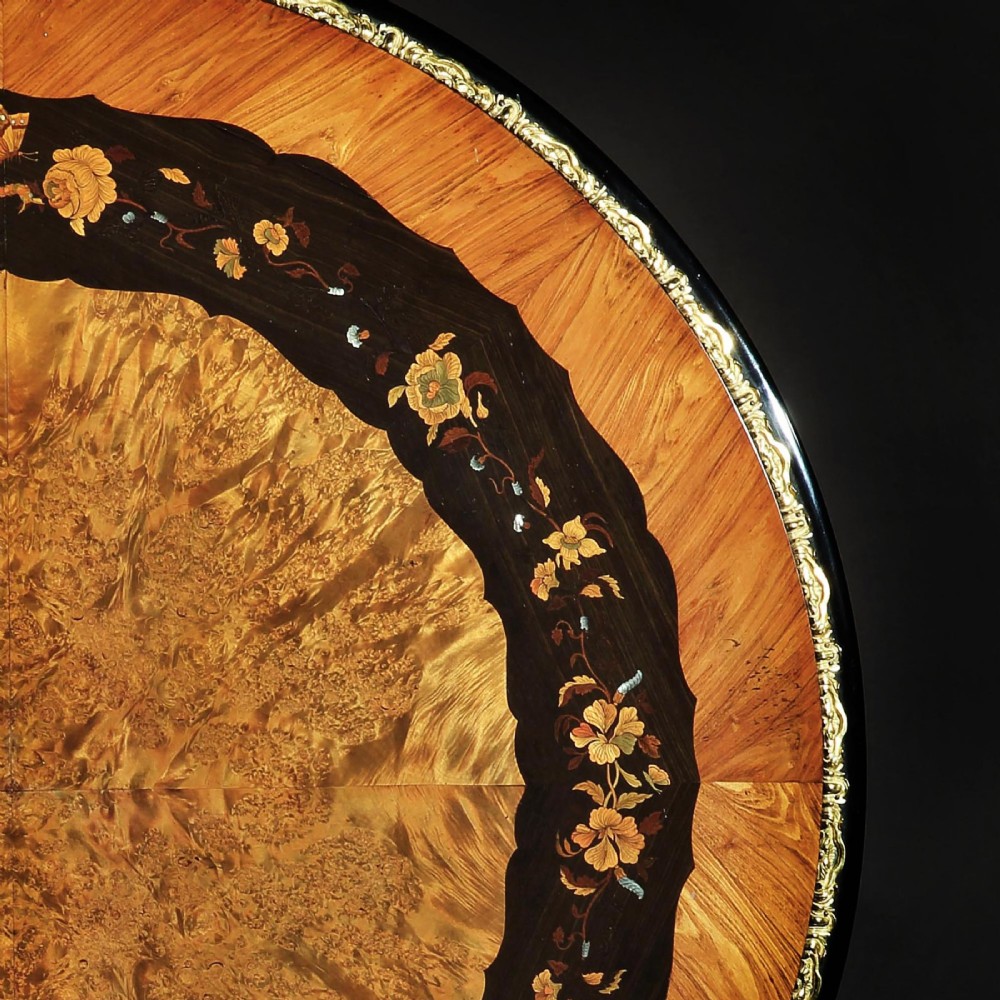 A 19th-century circular marquetry centre table featuring floral wood inlays, a tilt-top mechanism, and a dark carved tripod base with gilt-bronze mounts. View VI