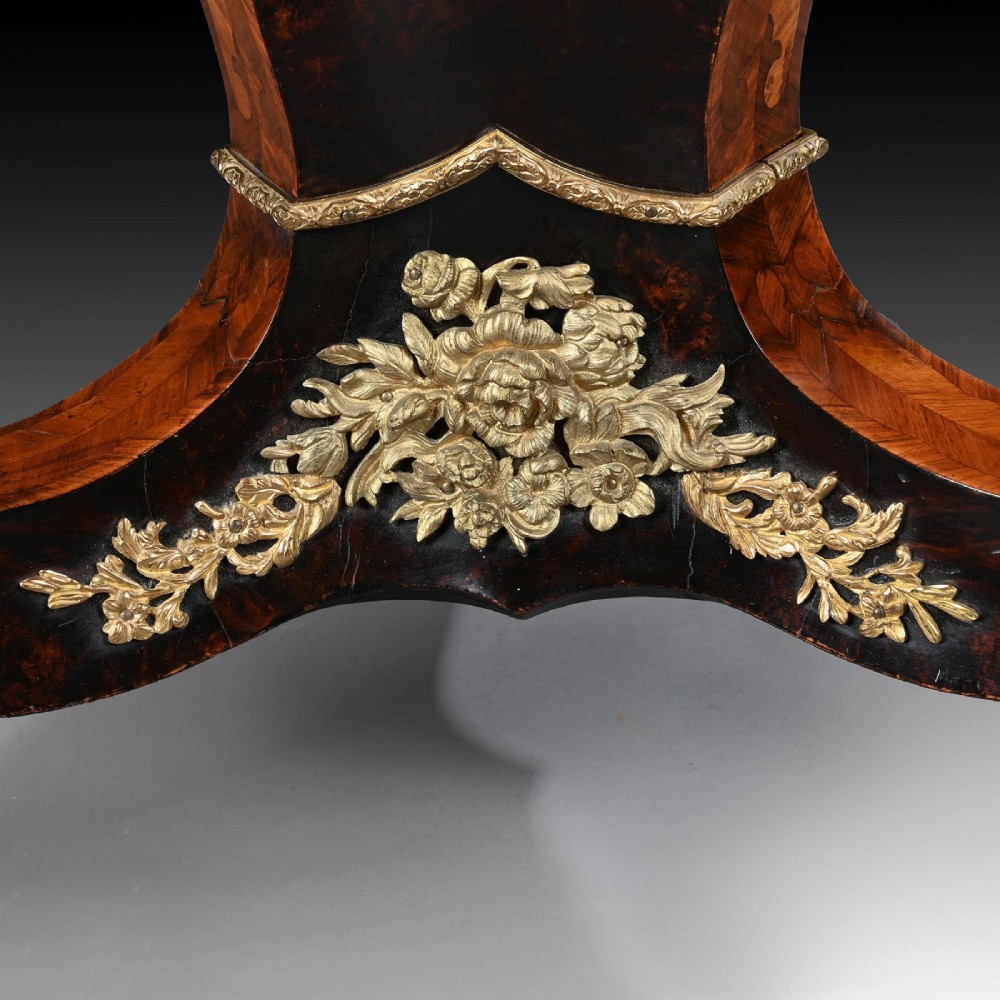A 19th-century circular marquetry centre table featuring floral wood inlays, a tilt-top mechanism, and a dark carved tripod base with gilt-bronze mounts. View VII