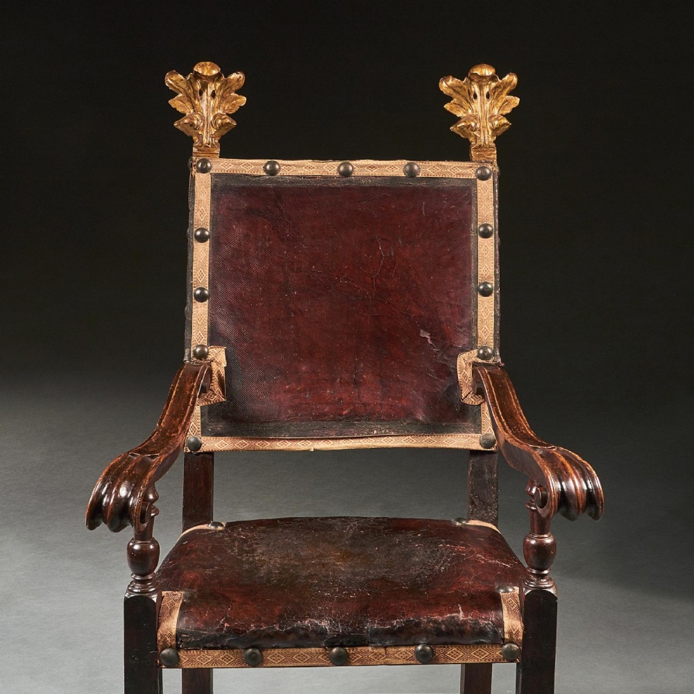 A pair of seventeenth-century Italian Baroque walnut armchairs featuring dark brown leather upholstery, decorative brass studs, turned stretchers, and gilded acanthus leaf finials. View V