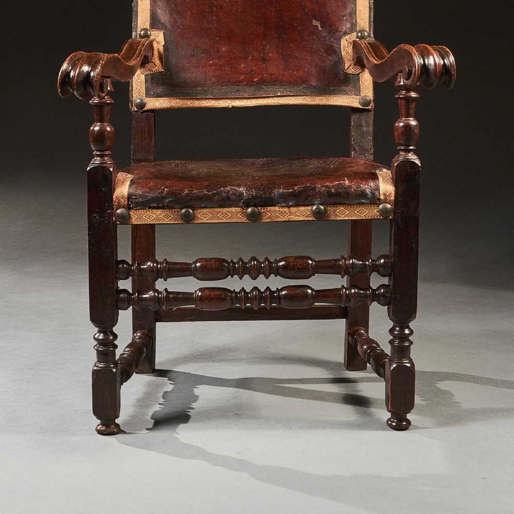 A pair of seventeenth-century Italian Baroque walnut armchairs featuring dark brown leather upholstery, decorative brass studs, turned stretchers, and gilded acanthus leaf finials. View VI