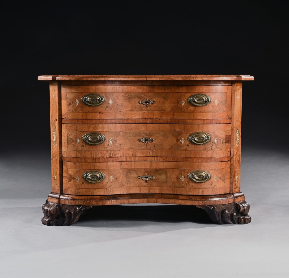 A mid-eighteenth-century German serpentine walnut commode featuring three drawers decorated with metal marquetry inlays, brass handles, and carved corner feet. View III