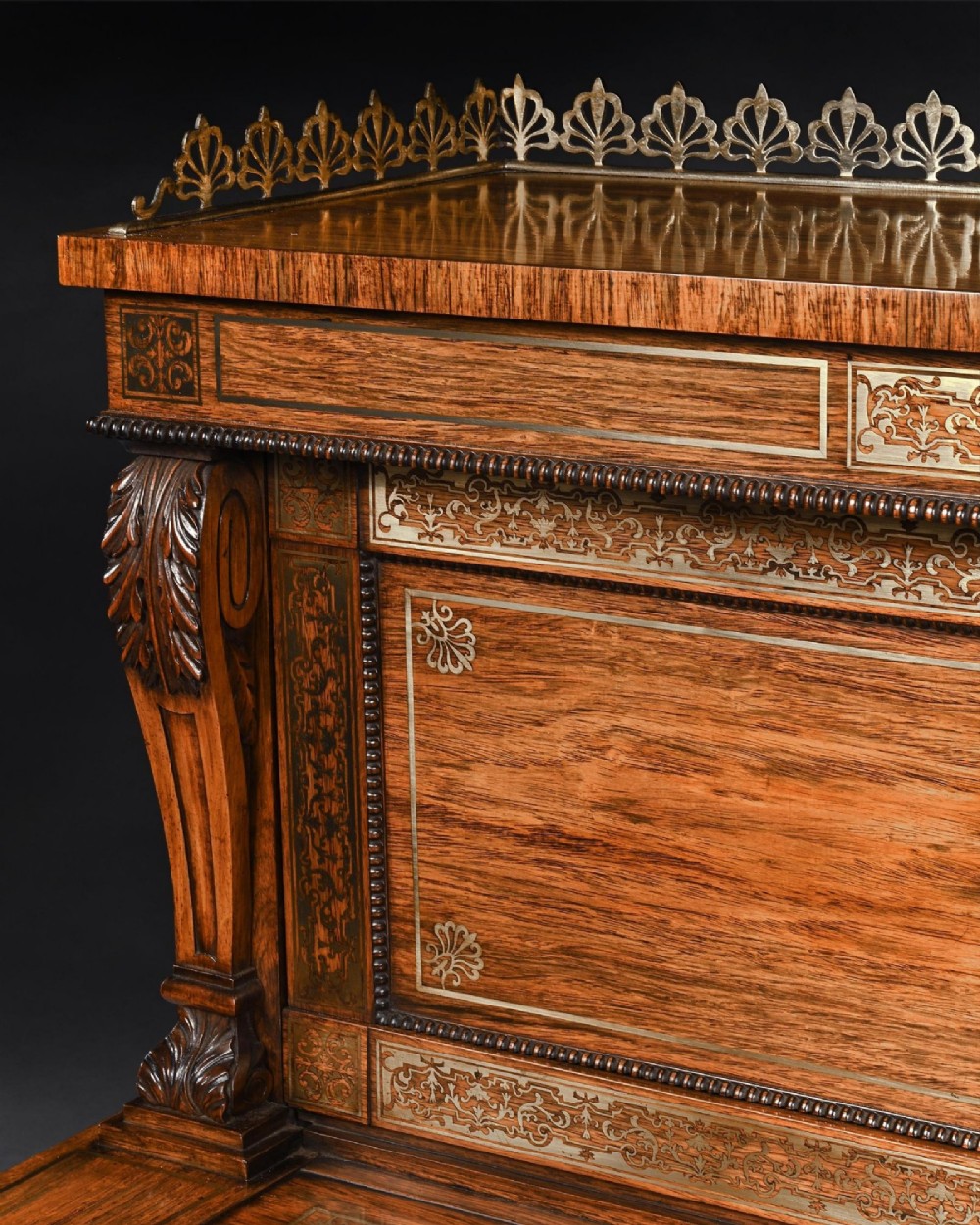 A Regency rosewood writing table featuring intricate brass scrollwork inlay, an anthemion top gallery, a central frieze drawer, and carved reeded legs. View IV