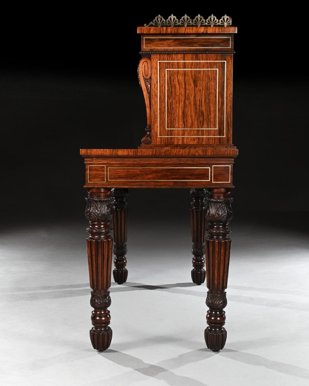 A Regency rosewood writing table featuring intricate brass scrollwork inlay, an anthemion top gallery, a central frieze drawer, and carved reeded legs. View VII