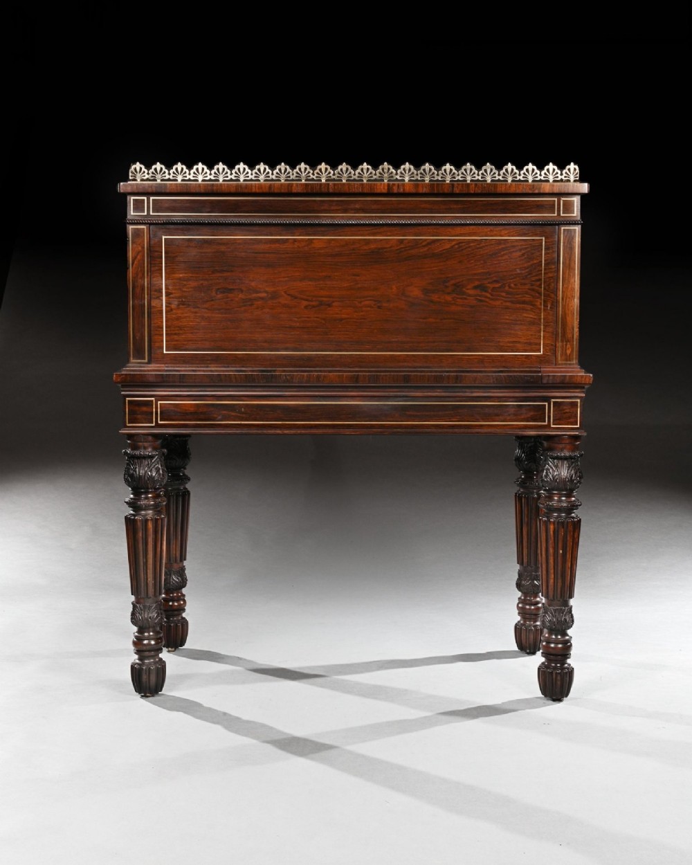 A Regency rosewood writing table featuring intricate brass scrollwork inlay, an anthemion top gallery, a central frieze drawer, and carved reeded legs. View VIII