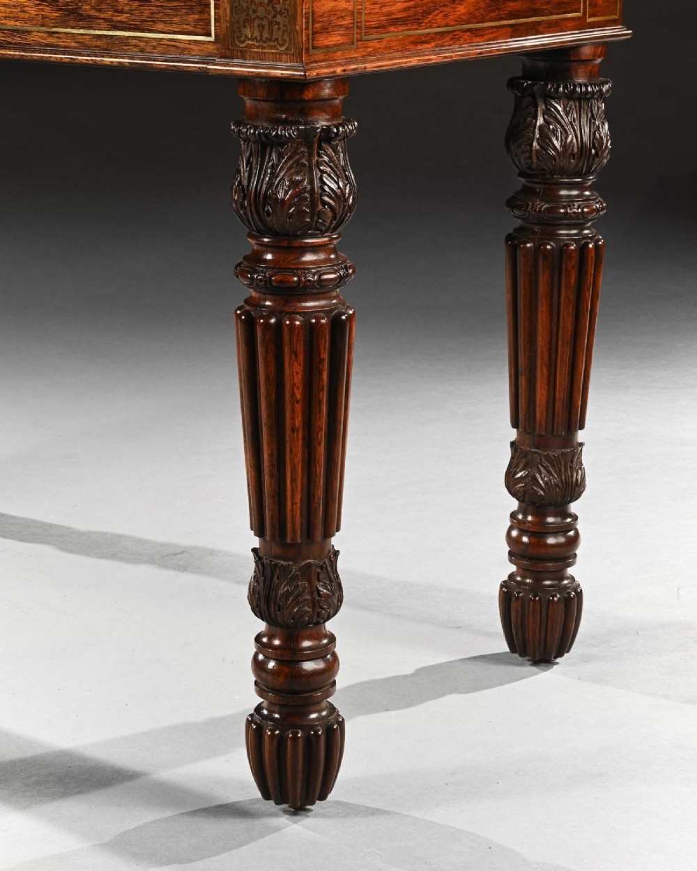 A Regency rosewood writing table featuring intricate brass scrollwork inlay, an anthemion top gallery, a central frieze drawer, and carved reeded legs. View IX