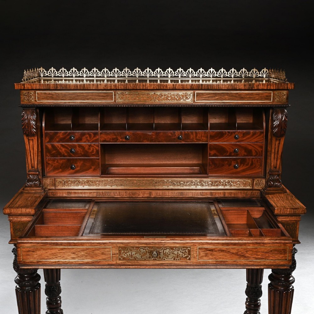 A Regency rosewood writing table featuring intricate brass scrollwork inlay, an anthemion top gallery, a central frieze drawer, and carved reeded legs. View X