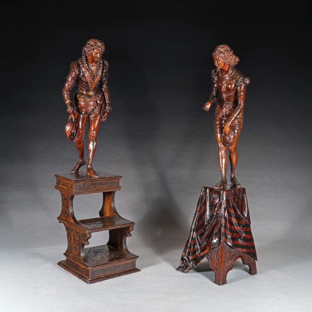 A pair of carved brown wood figures depicting Renaissance figures atop detailed wooden bases.