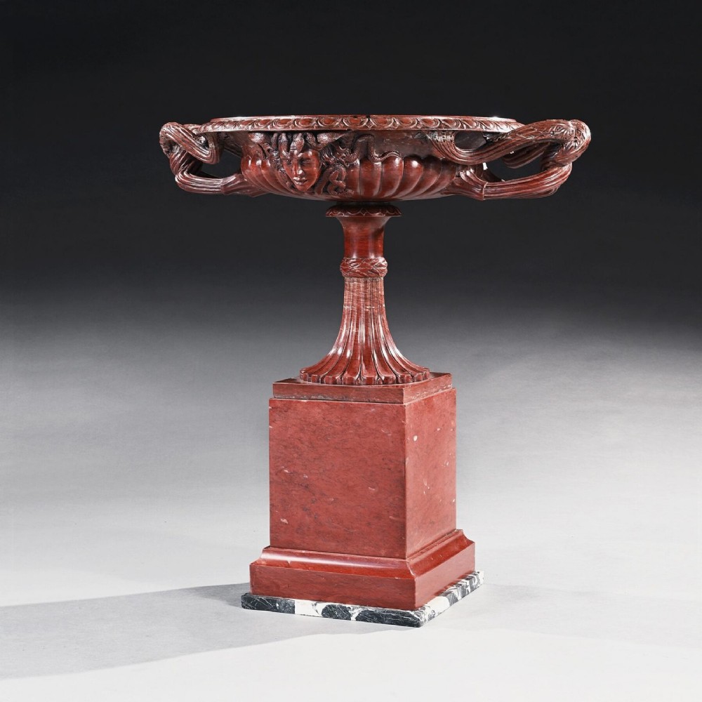 A carved deep red Rosso Antico marble tazza featuring serpent handles, a Medusa mask motif, and a fluted stem set upon a square pedestal base.
