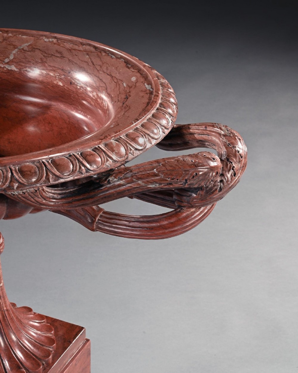 A carved deep red Rosso Antico marble tazza featuring serpent handles, a Medusa mask motif, and a fluted stem set upon a square pedestal base. View VII