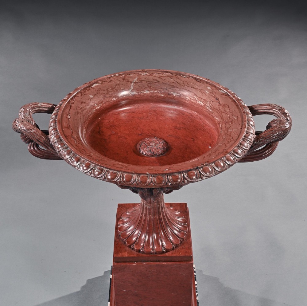 A carved deep red Rosso Antico marble tazza featuring serpent handles, a Medusa mask motif, and a fluted stem set upon a square pedestal base. View VIII