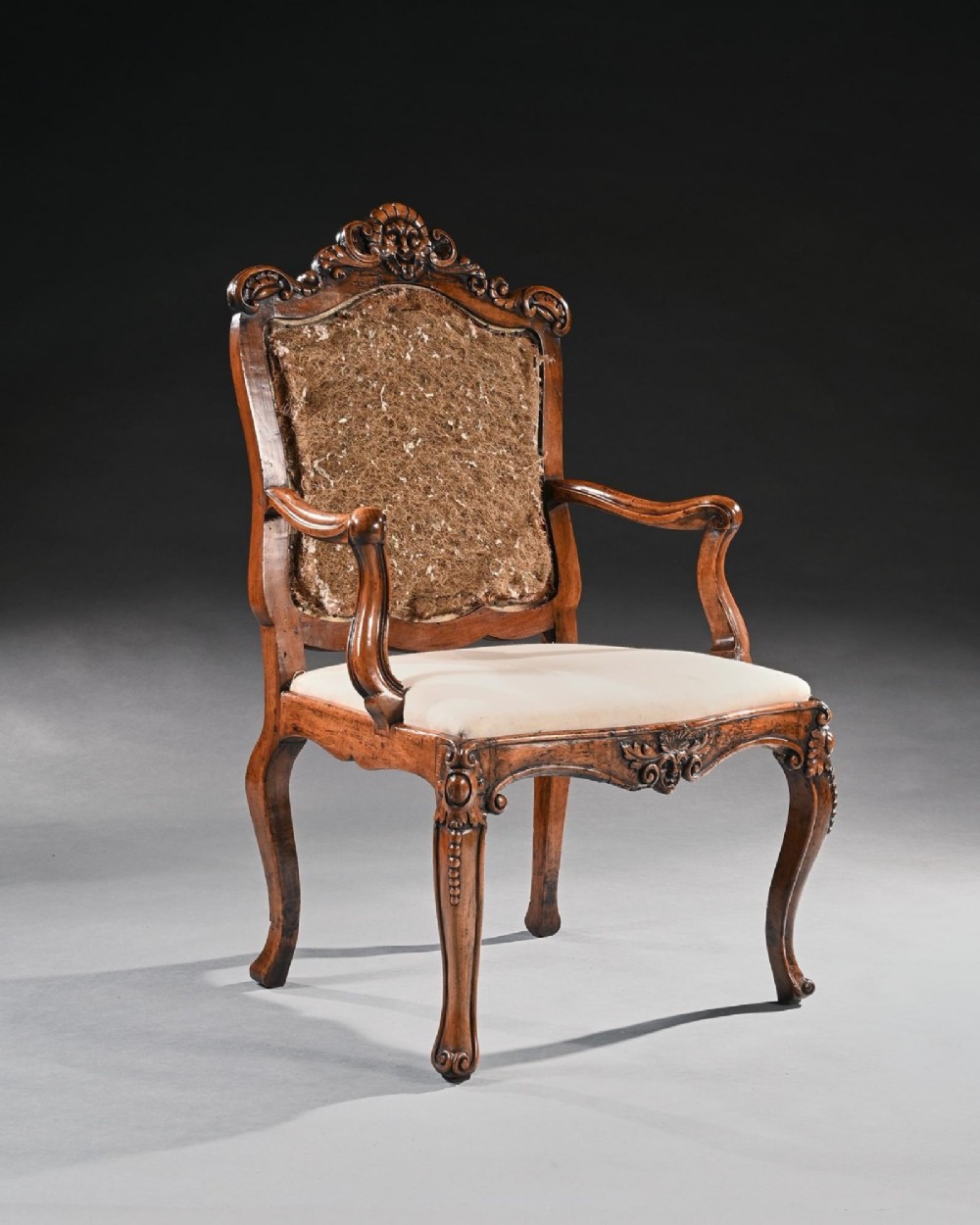 Mid-18th-century Italian Rococo carved walnut armchair featuring cabriole legs, curved armrests, an ornate carved mask crest rail, and exposed traditional back padding. View III