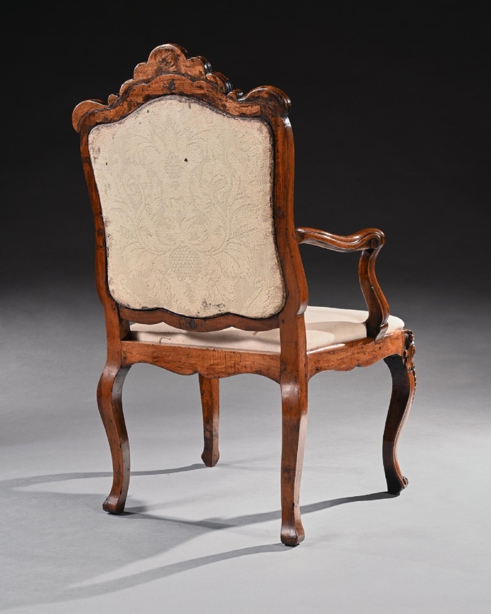 Mid-18th-century Italian Rococo carved walnut armchair featuring cabriole legs, curved armrests, an ornate carved mask crest rail, and exposed traditional back padding. View IV