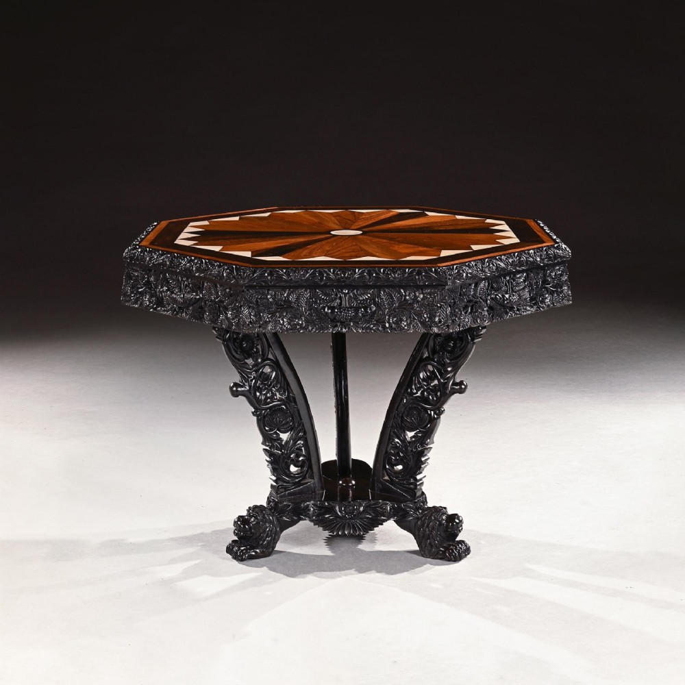 A 19th-century Ceylonese octagonal centre table crafted from dark ebony featuring a geometric starburst specimen wood inlaid top and deeply carved pedestal base. View II