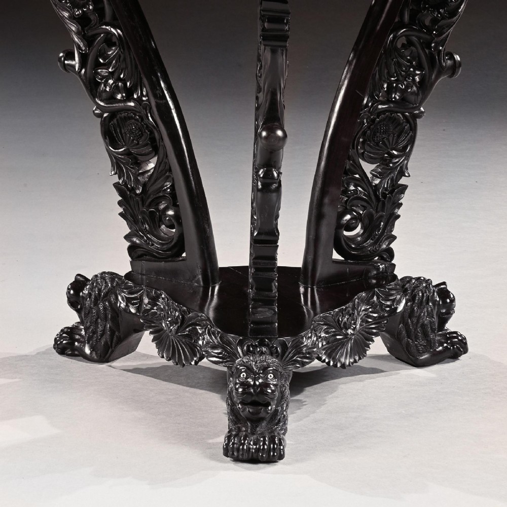 A 19th-century Ceylonese octagonal centre table crafted from dark ebony featuring a geometric starburst specimen wood inlaid top and deeply carved pedestal base. View IV