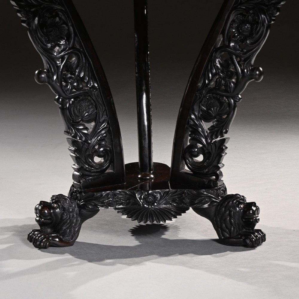 A 19th-century Ceylonese octagonal centre table crafted from dark ebony featuring a geometric starburst specimen wood inlaid top and deeply carved pedestal base. View V