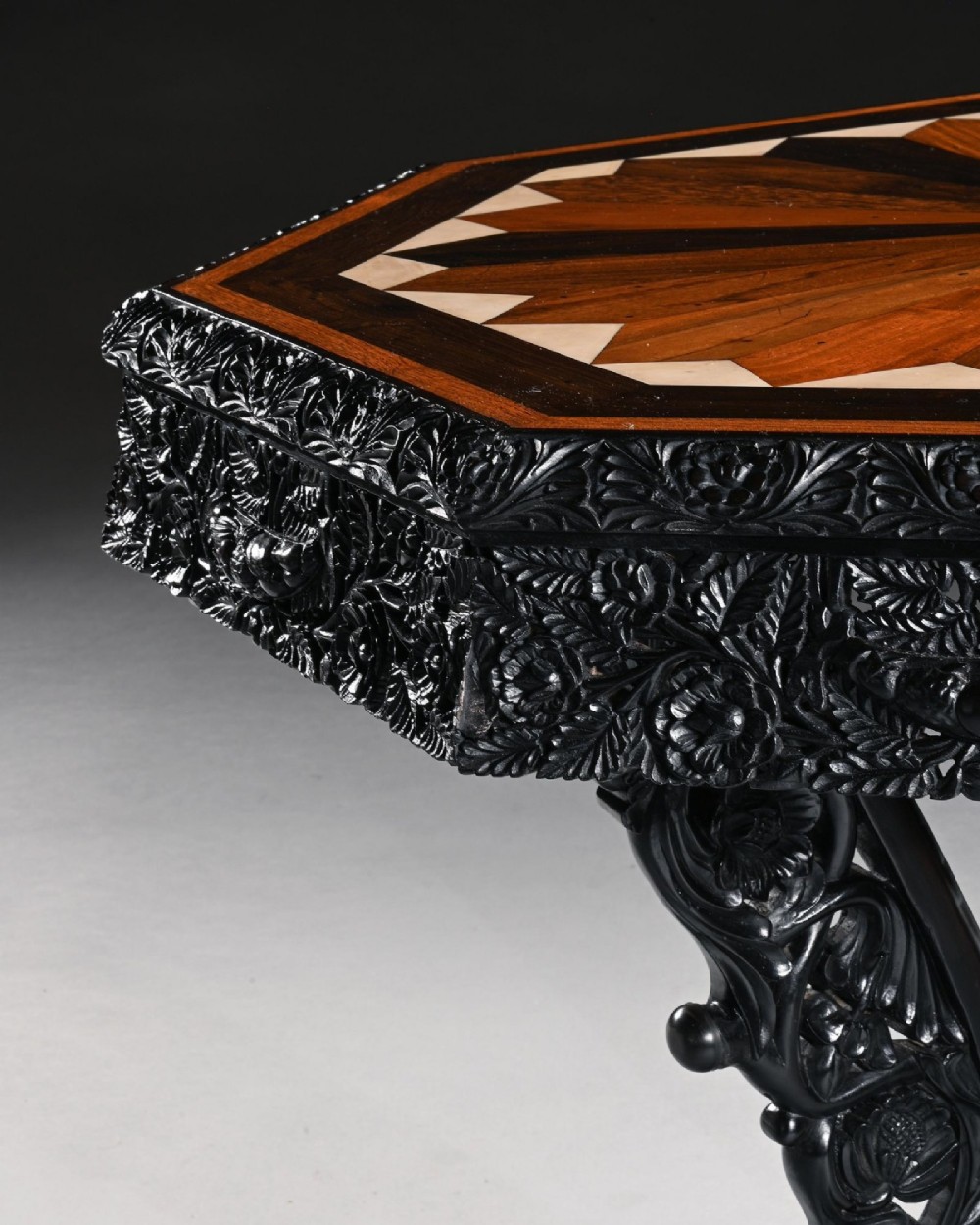 A 19th-century Ceylonese octagonal centre table crafted from dark ebony featuring a geometric starburst specimen wood inlaid top and deeply carved pedestal base. View VII