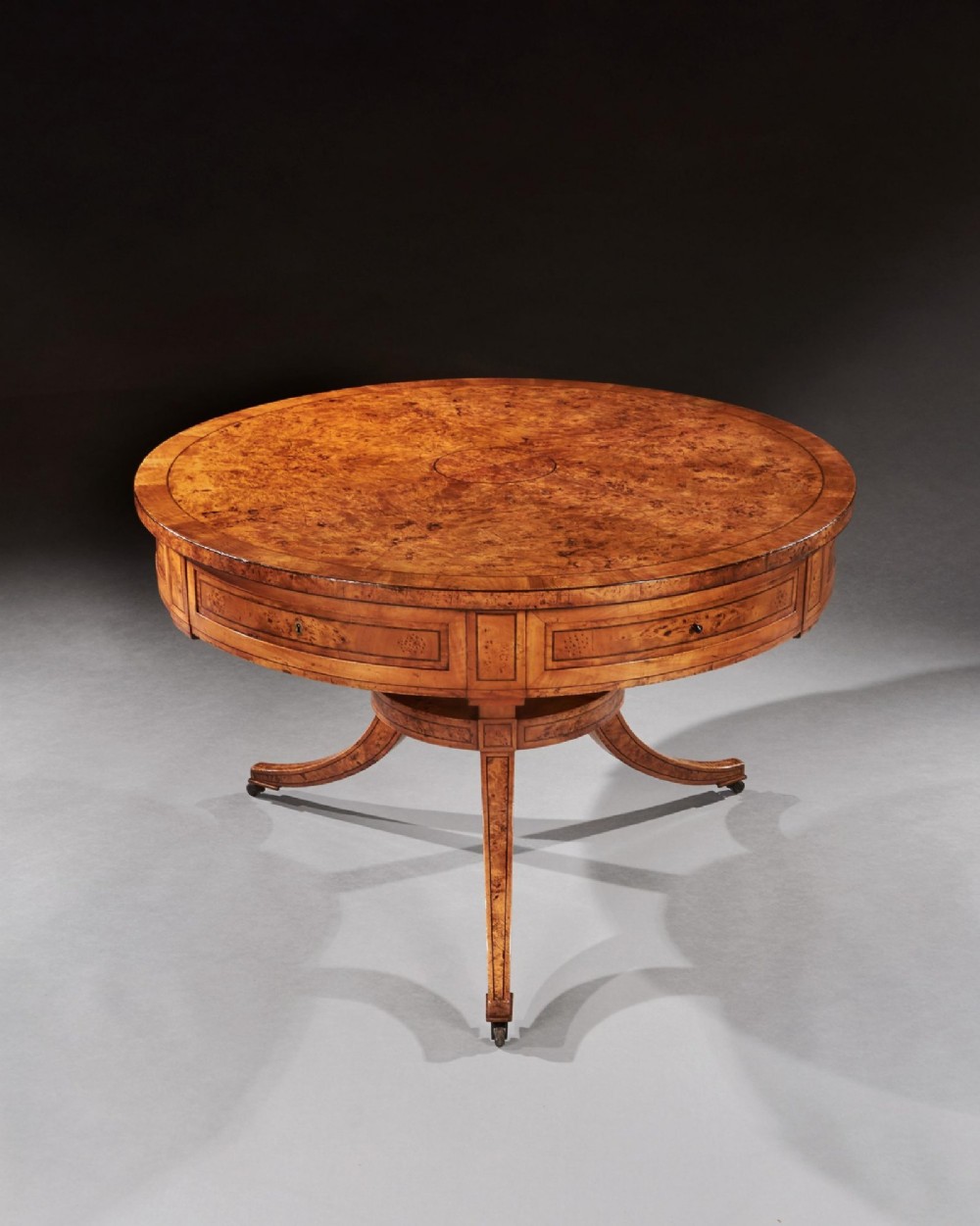 A circular early 19th-century Scandinavian drum table crafted from burr maple with frieze drawers, a lower shelf, and quadruped splayed legs with brass castors. View II