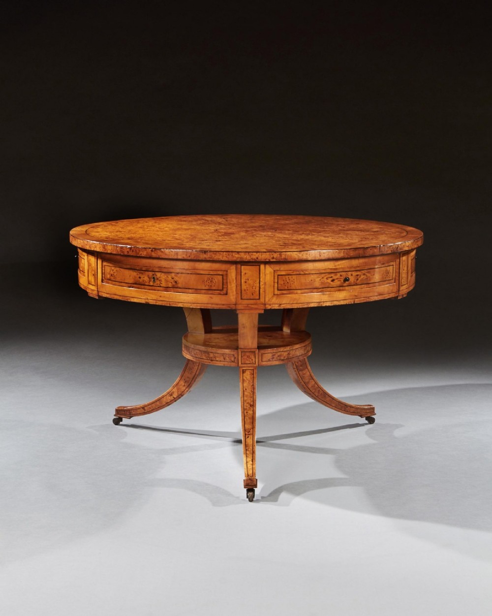 A circular early 19th-century Scandinavian drum table crafted from burr maple with frieze drawers, a lower shelf, and quadruped splayed legs with brass castors. View III