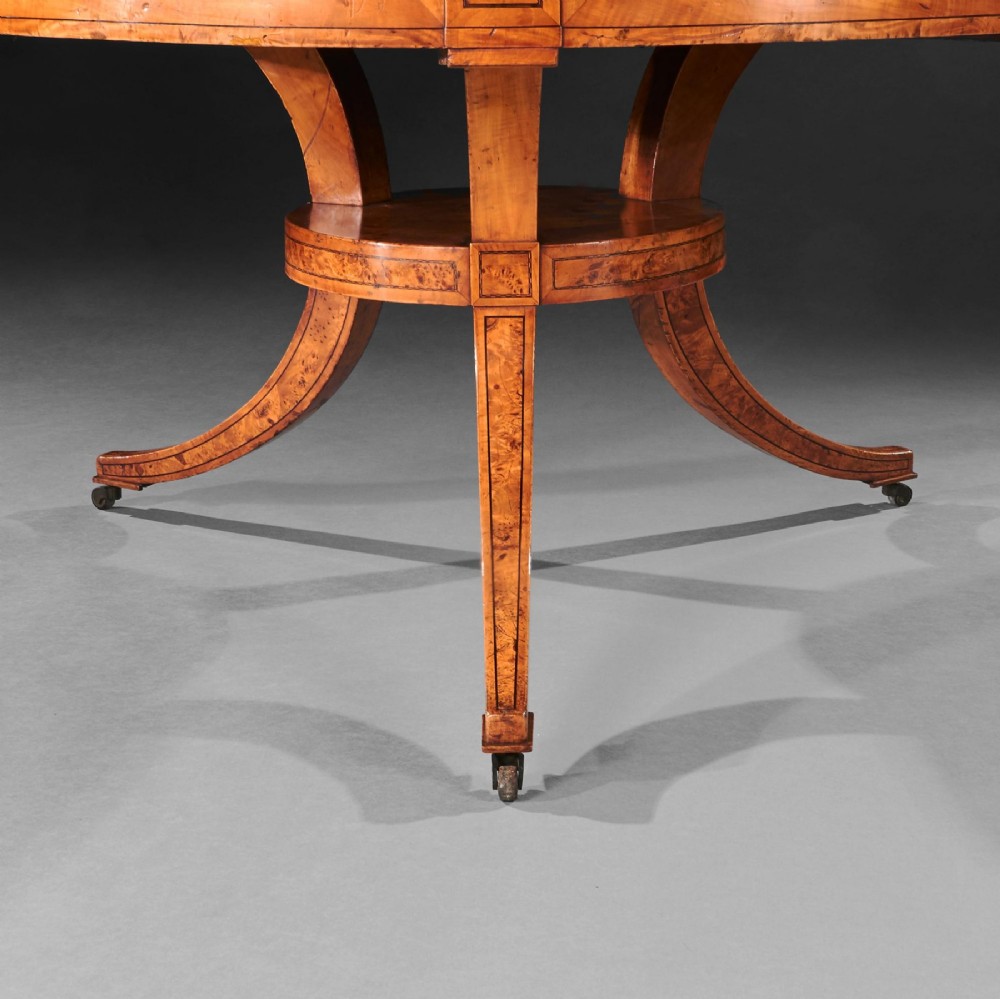 A circular early 19th-century Scandinavian drum table crafted from burr maple with frieze drawers, a lower shelf, and quadruped splayed legs with brass castors. View VII