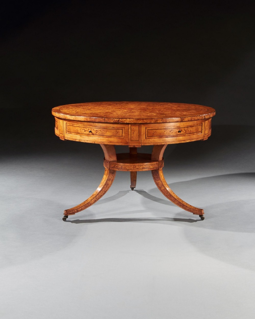 A circular early 19th-century Scandinavian drum table crafted from burr maple with frieze drawers, a lower shelf, and quadruped splayed legs with brass castors. View IX