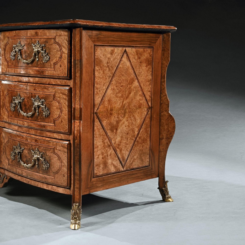 An 18th-century French Regence commode crafted from burr maple veneer featuring three drawers with detailed gilt-bronze handles, keyhole escutcheons, and foot mounts. View V