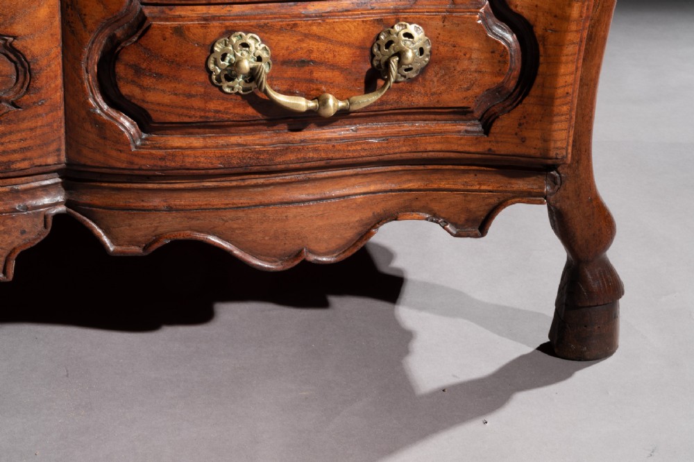 A mid-18th century French Louis XV provincial bombee commode in warm chestnut wood, featuring three carved panel drawers with ornamental brass handles. View XI