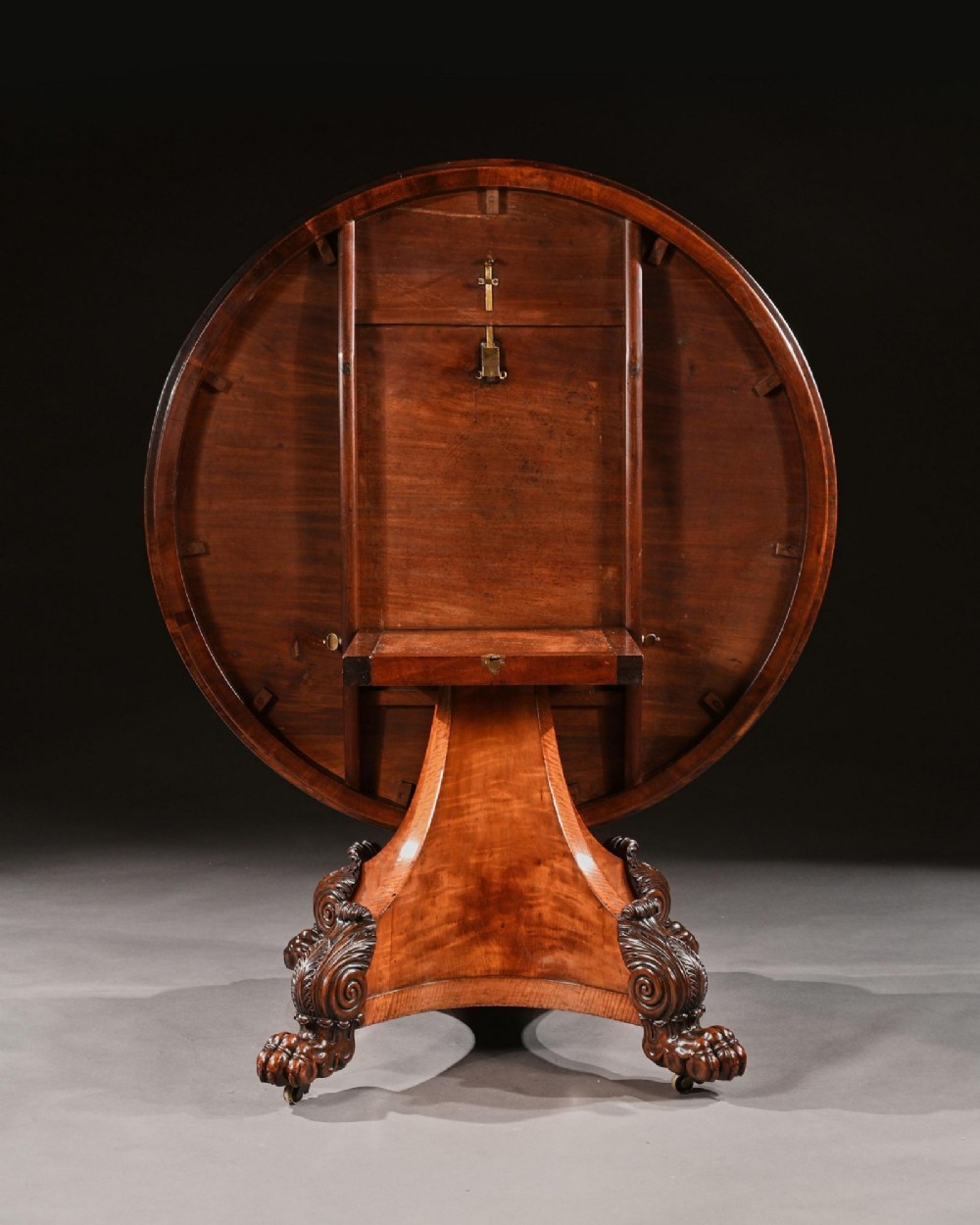 A circular 19th-century satinwood centre table with rosewood crossbanding, supported by a flared triangular pedestal base and carved scroll feet. View VIII