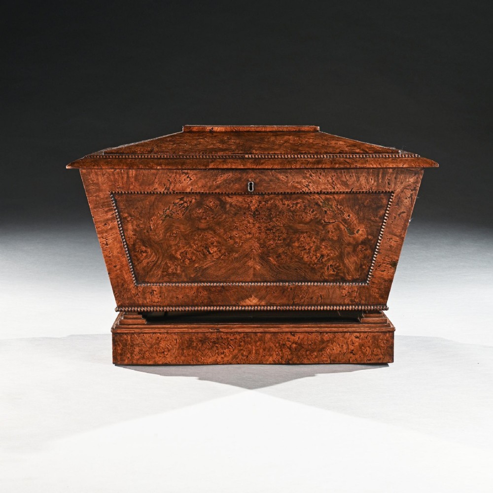 A Regency period sarcophagus-form cellarette crafted from burr pollard oak timber featuring a hinged lid, bead moulding, and a plinth base. View III