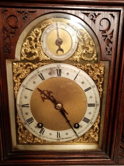 fig 1. A large dark carved oak bracket clock featuring a decorative scale-patterned dome topped with a central finial, fluted side columns, and an ornate brass dial with a silvered chapter ring.