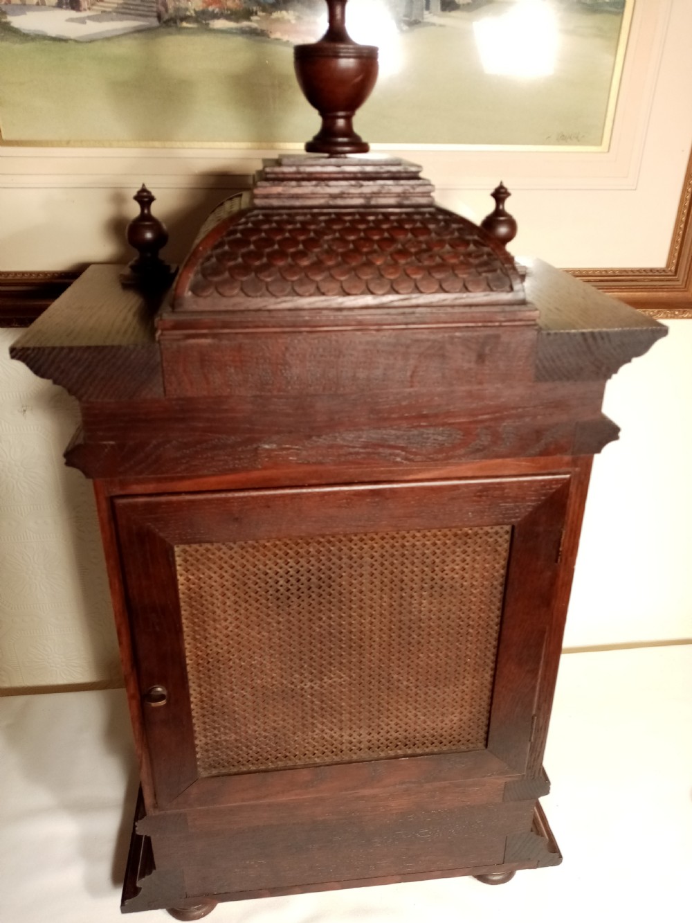 A large dark carved oak bracket clock featuring a decorative scale-patterned dome topped with a central finial, fluted side columns, and an ornate brass dial with a silvered chapter ring. View VIII