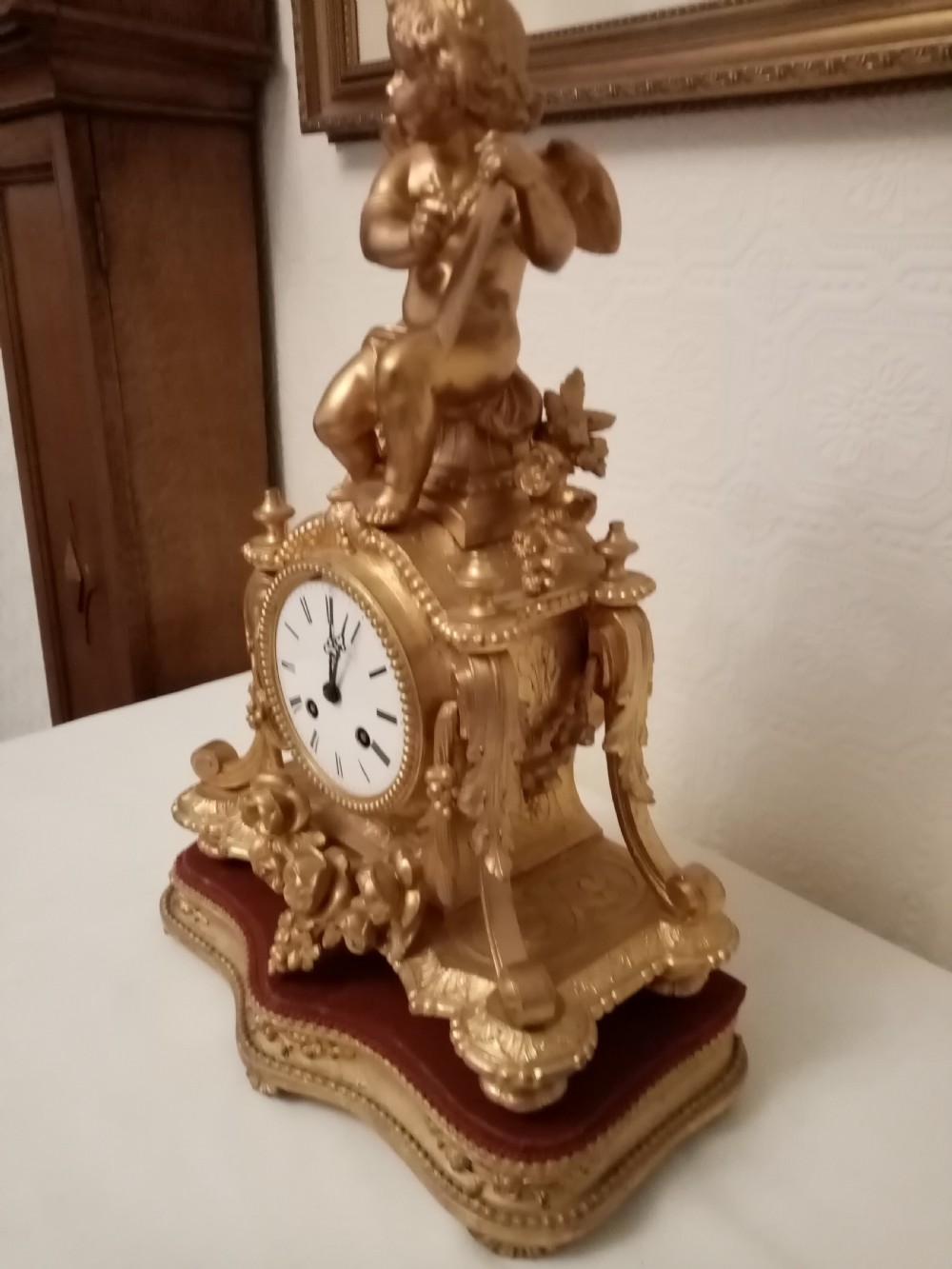 An ornate gold gilt bronze mantel clock topped with a seated cherub figure writing on a scroll above an enamelled dial with Roman numerals. View II