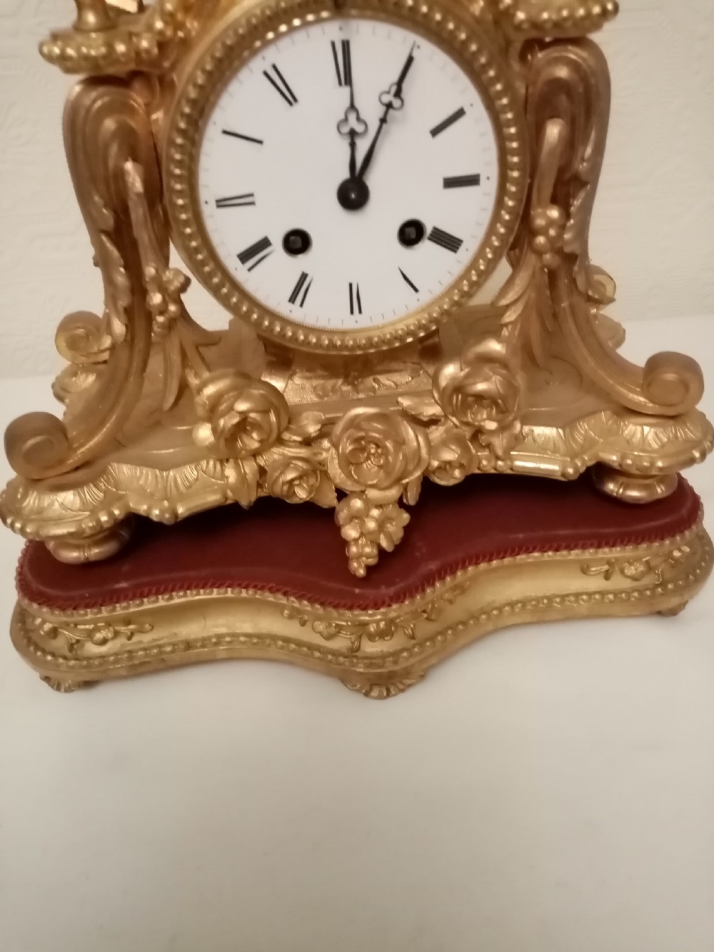 An ornate gold gilt bronze mantel clock topped with a seated cherub figure writing on a scroll above an enamelled dial with Roman numerals. View VII