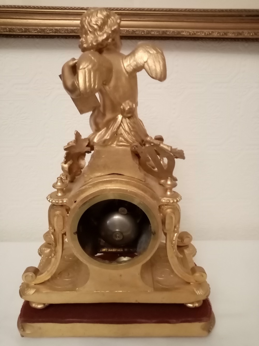 An ornate gold gilt bronze mantel clock topped with a seated cherub figure writing on a scroll above an enamelled dial with Roman numerals. View IX