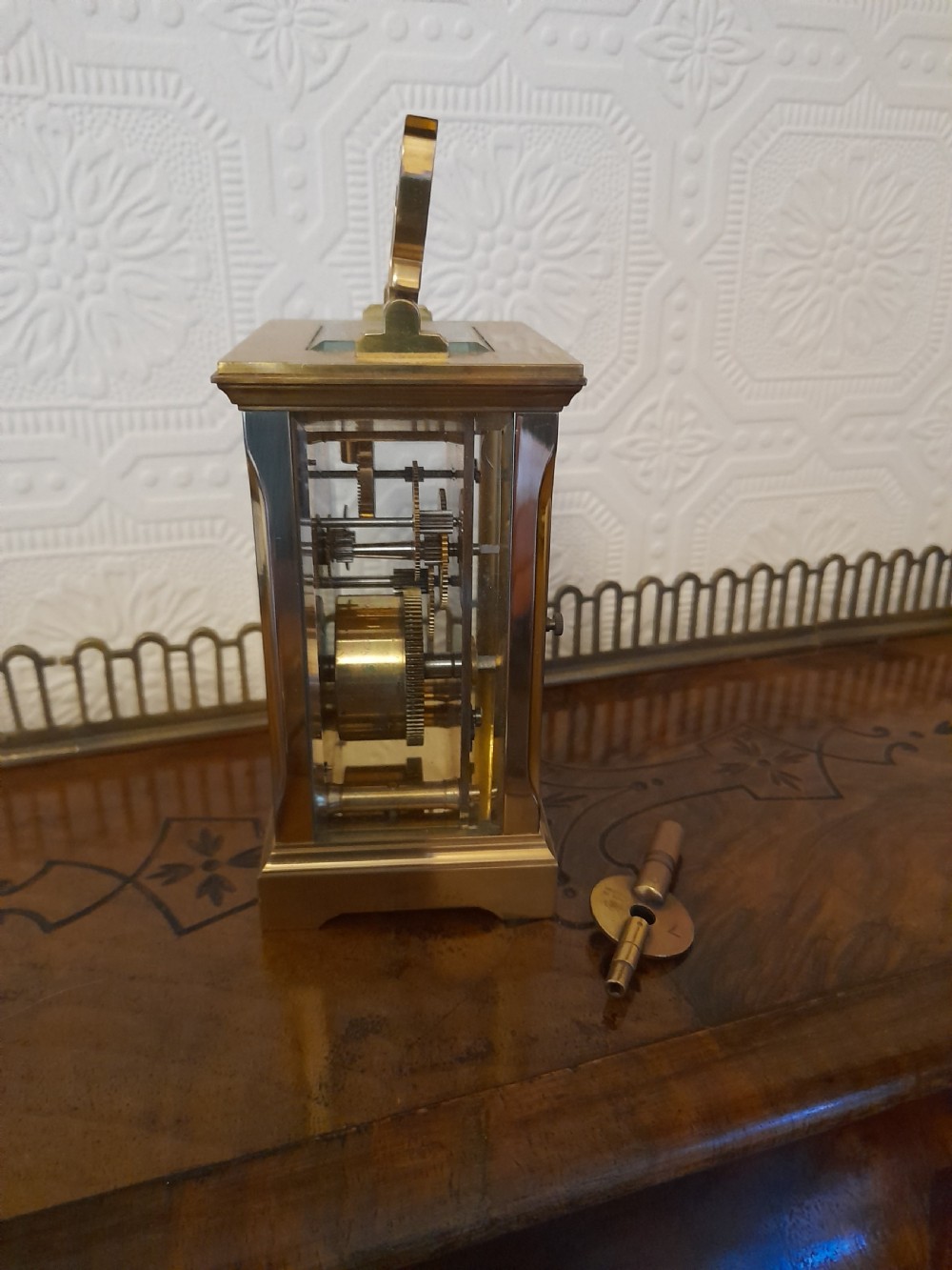 A rectangular brass carriage clock featuring clear glass side panels, a white enamel dial with black Roman numerals, and a shaped brass carrying handle. View V