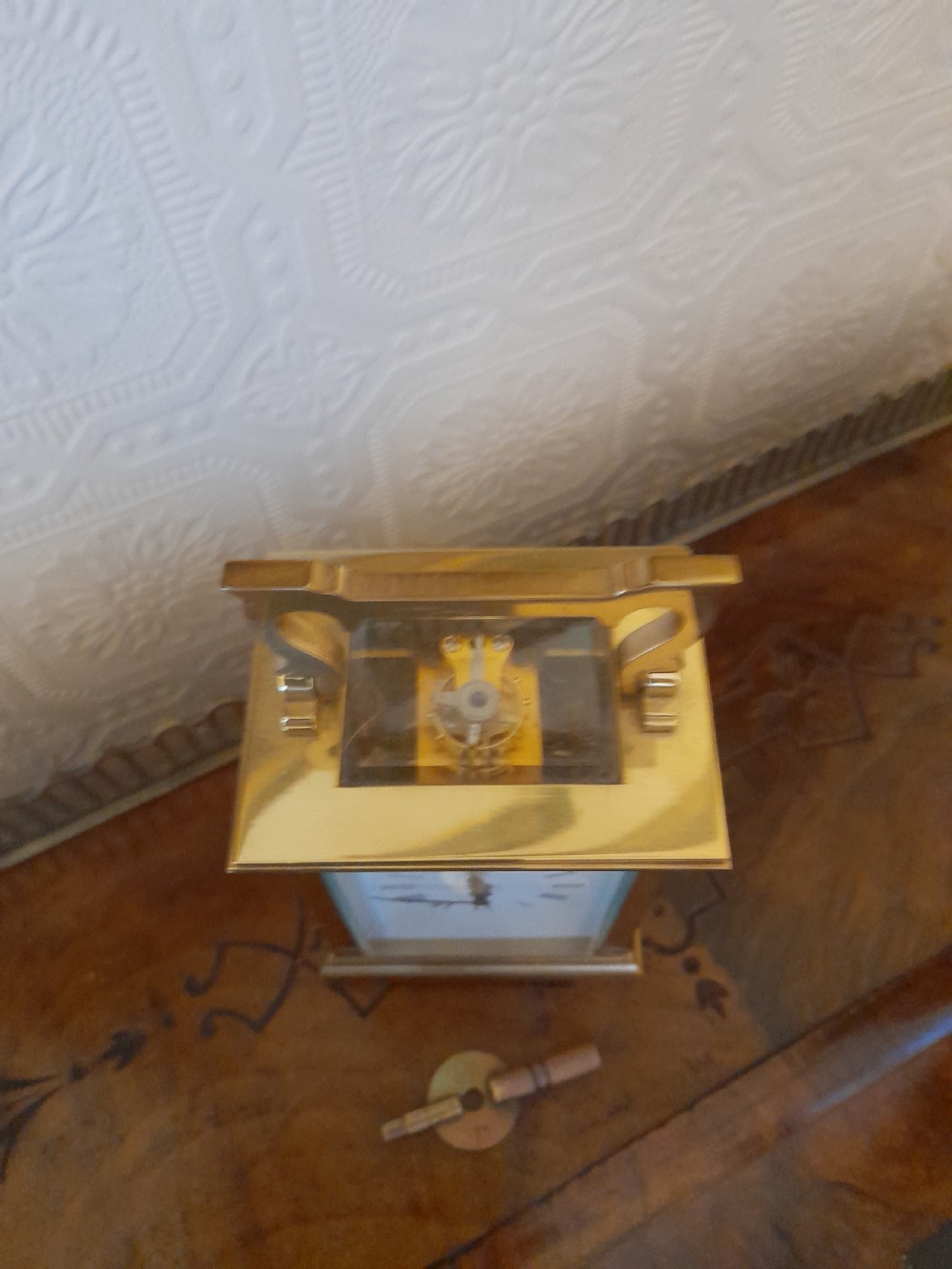 A rectangular brass carriage clock featuring clear glass side panels, a white enamel dial with black Roman numerals, and a shaped brass carrying handle. View VIII