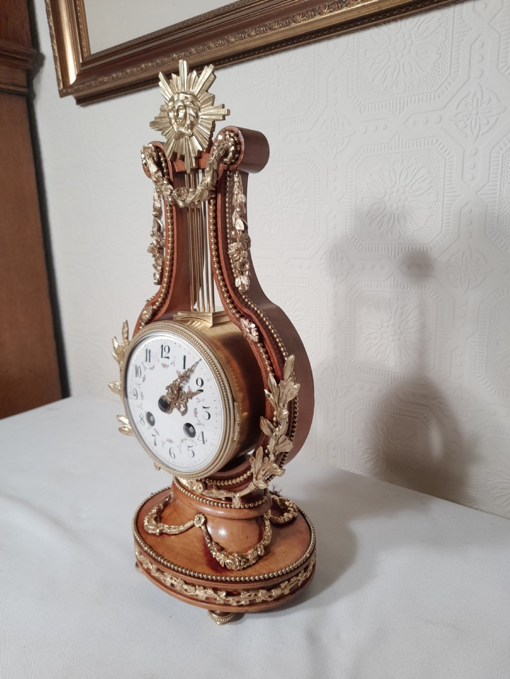 A Louis XVI style wooden lyre clock featuring gilt bronze floral mounts, a sunburst mask finial, and a white enamel dial. View II
