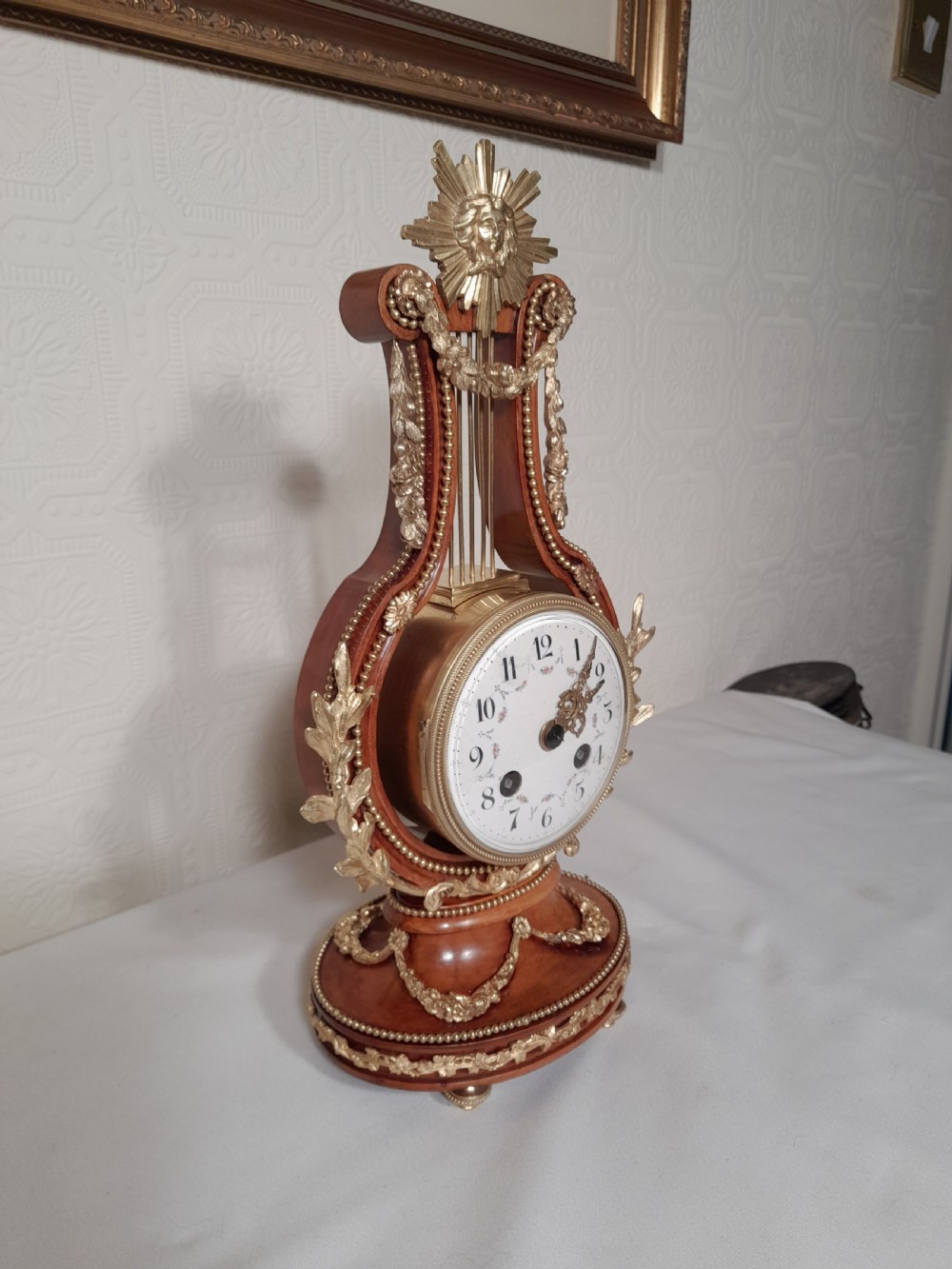 A Louis XVI style wooden lyre clock featuring gilt bronze floral mounts, a sunburst mask finial, and a white enamel dial. View III